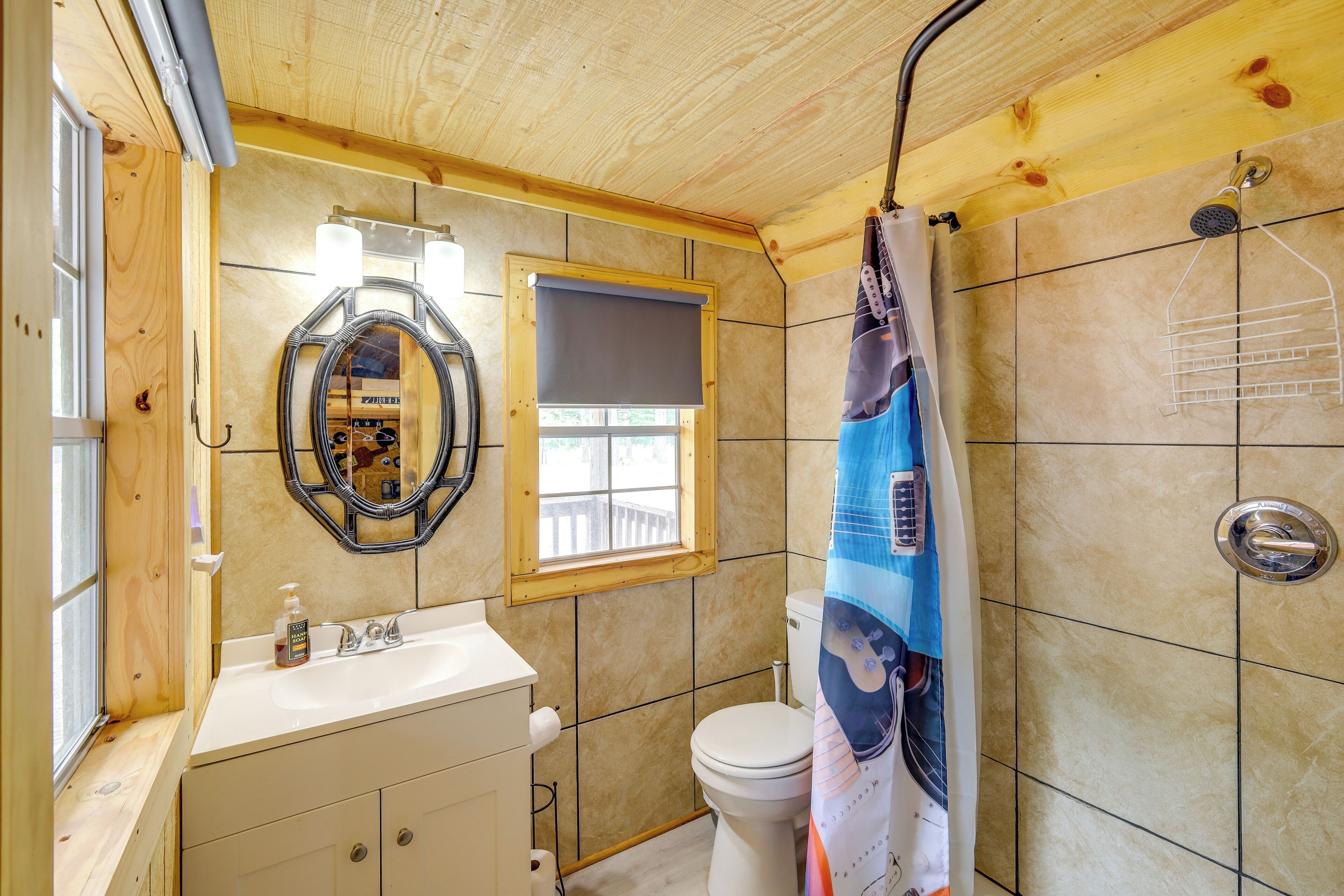A bathroom with a wooden ceiling, a white sink, a toilet, a mirror, and a shower curtain.