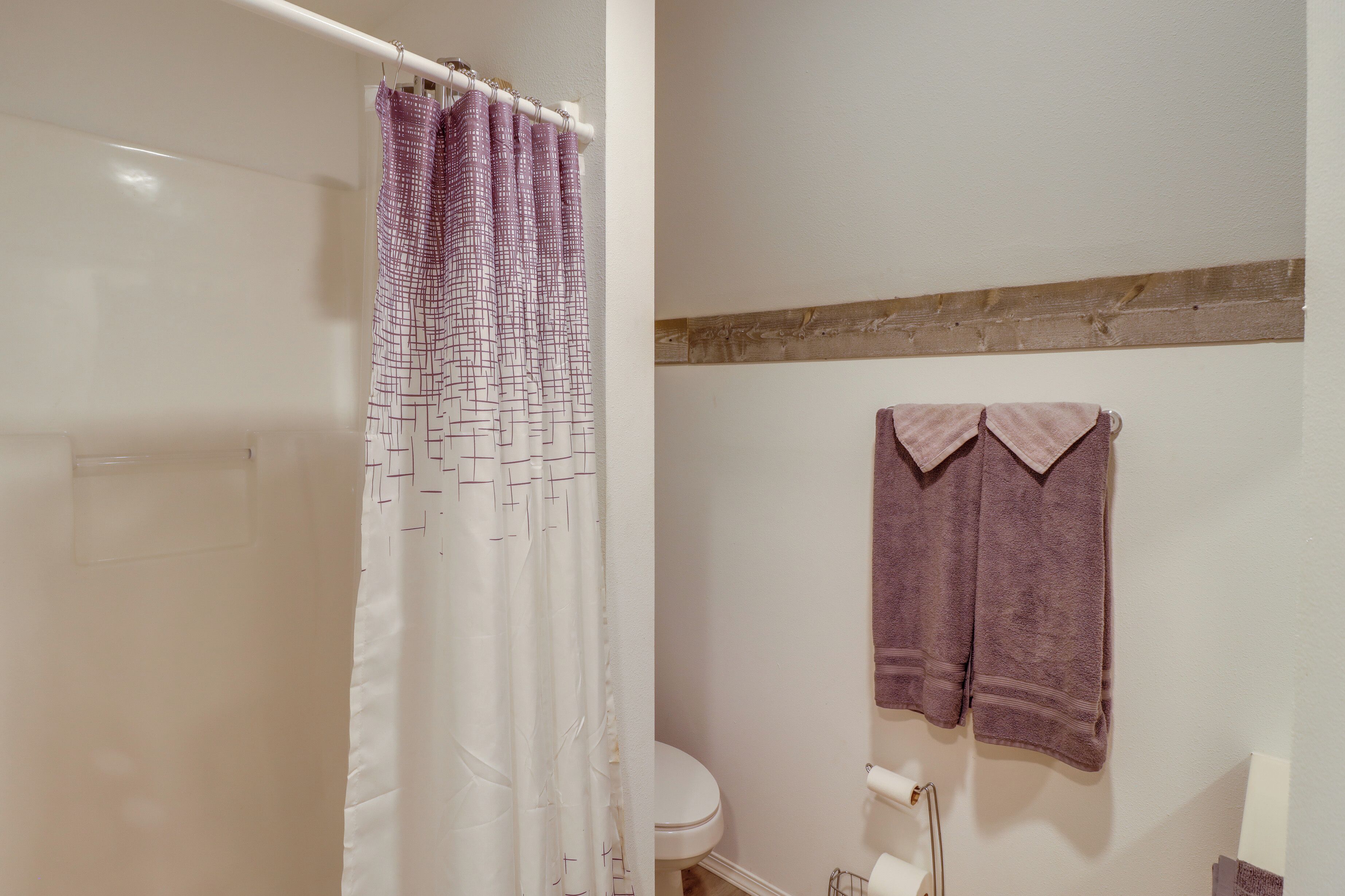 A bathroom with a shower curtain, a toilet, and two towels hanging on the wall.