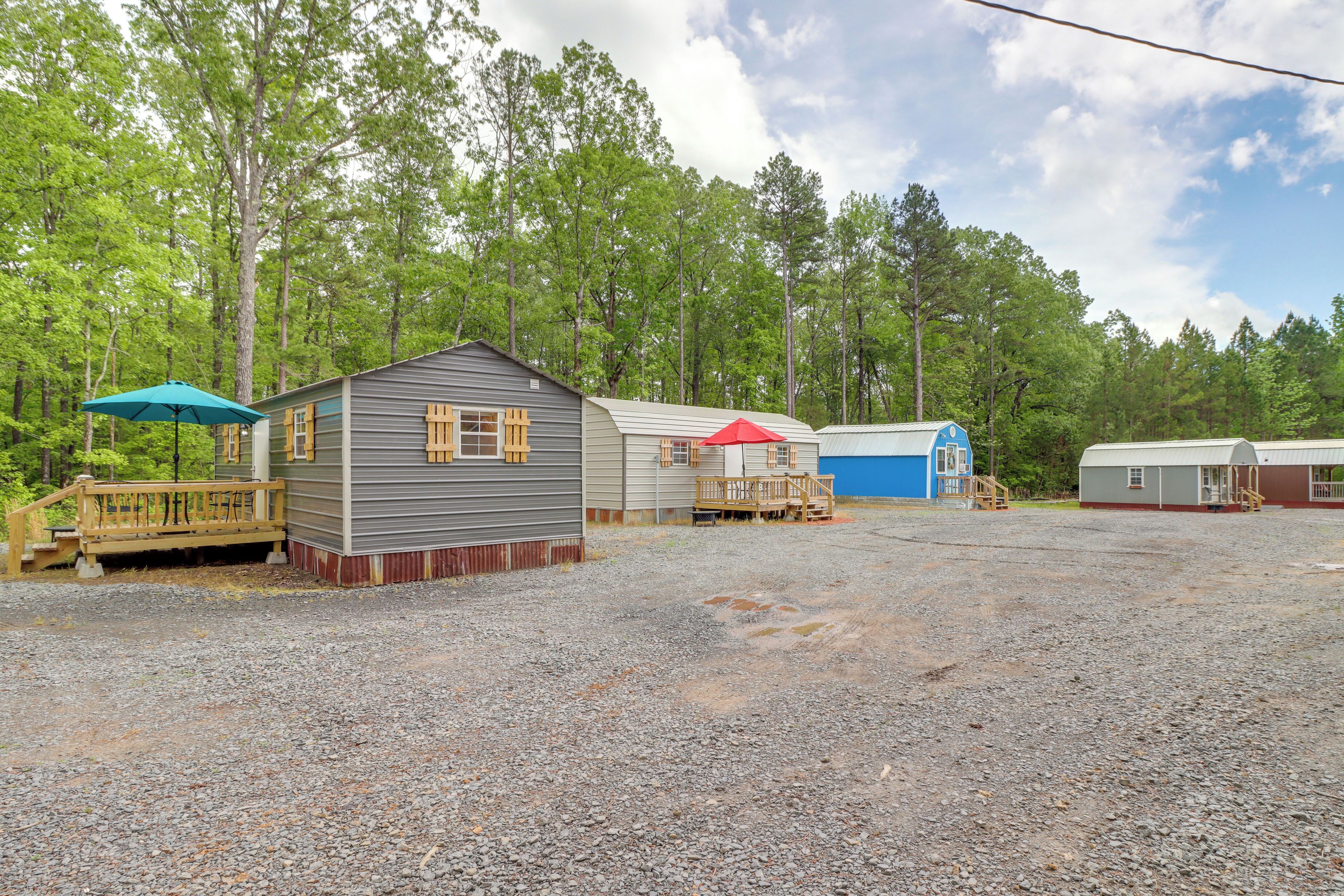 A campground with several cabins, a gravel parking area, and a wooden deck with a blue umbrella.