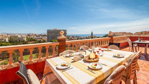 Una terraza con mesa lista para comer, con vistas a la ciudad y al mar.