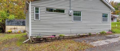 A single-story house with a gabled roof, a front porch with a wooden railing, and a small garden with flowers.