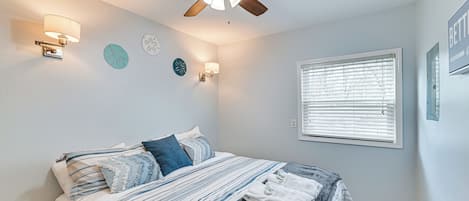 A bedroom with a bed, ceiling fan, wall sconces, and a window with blinds.