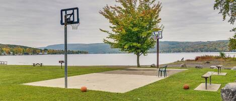 A park with a basketball court, picnic tables, and a view of a lake.