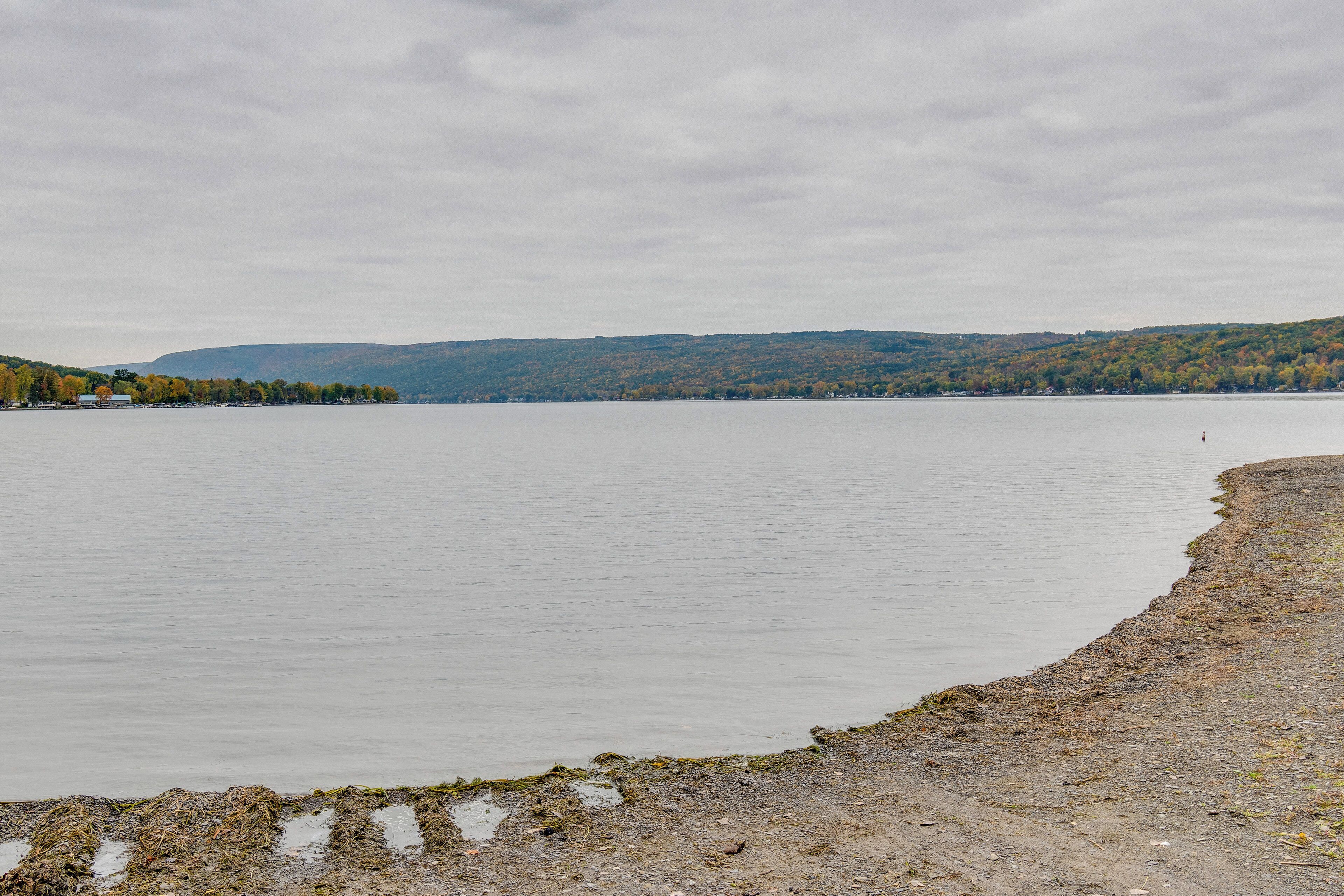 Ein ruhiger See mit steiniger Uferlinie und sanften Hügeln im Hintergrund.