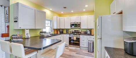 A modern kitchen with white cabinets, a central island with bar stools, stainless steel appliances, and a tiled floor.