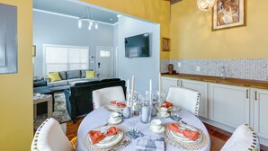 A dining area with a round table set for four, surrounded by white chairs. There is a sofa and a television in the background. - Inviting Quincy Cottage: Walk to Historic Downtown (Quincy)