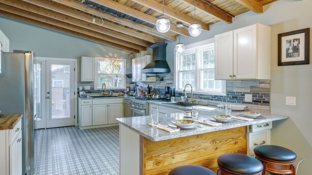 A spacious kitchen with a large island, wooden bar stools, and a view of the backyard through the sliding glass door. - Inviting Quincy Cottage: Walk to Historic Downtown (Quincy)