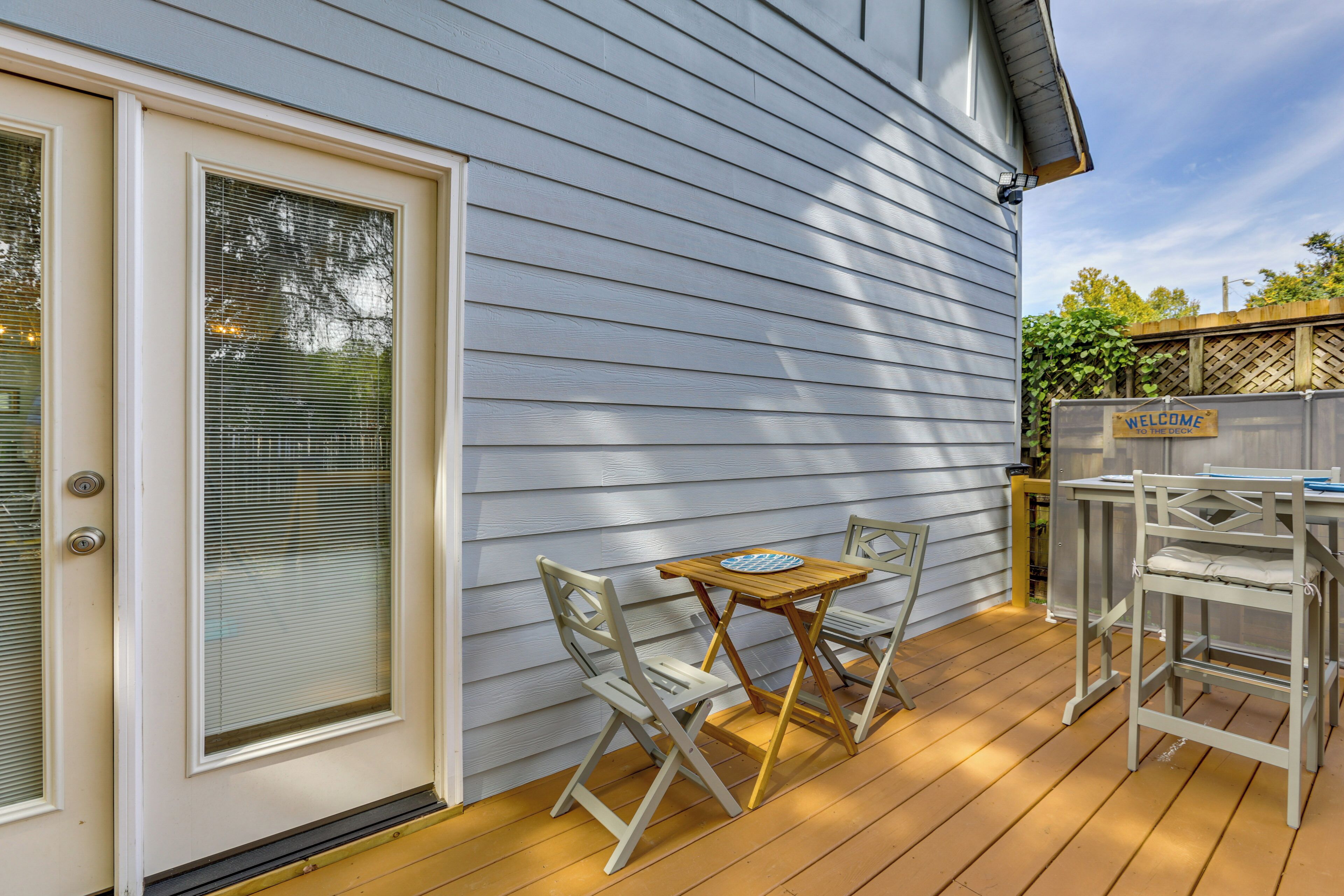 A wooden deck with a table and chairs, a door with a window, and a welcome sign.
