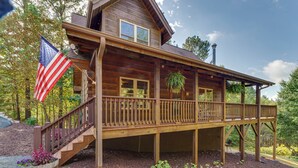 A wooden cabin with a deck, a flag, and a garden area. - Deck, Grill & Fire Pit: Blue Ridge Mountain Cabin! (Bostic)