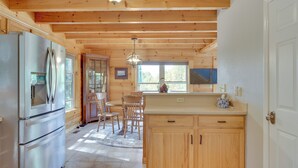 A wooden cabin interior with a kitchen area featuring a refrigerator, wooden cabinets, and a dining table with chairs. - Deck, Grill & Fire Pit: Blue Ridge Mountain Cabin! (Bostic)