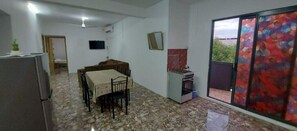 A compact kitchen with a dining table, a refrigerator, and a small stove. There is a sliding glass door leading to a balcony. - Bungalow 7 en Bord de mer Mont Choisy (Trou-aux-Biches)