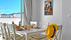 A dining area with a table set for breakfast, chairs, a yellow hat, and a painting on the wall. - Ferienwohnung Ocean Sounds A in Gran Tarajal, Innenstadt, Meerblick, Terrasse (Gran Tarajal)