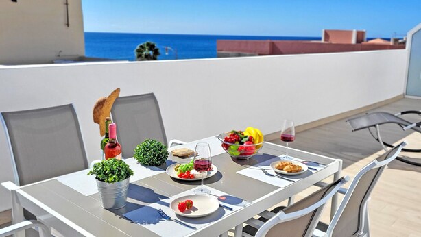 A dining table with chairs, a hanging chair, and a view of the sea. - Ferienwohnung Ocean Sounds A in Gran Tarajal, Innenstadt, Meerblick, Terrasse (Gran Tarajal)