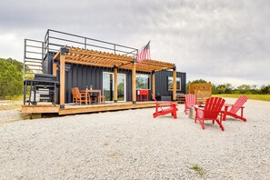 A modern outdoor seating area with a pergola, red Adirondack chairs, and a grill.