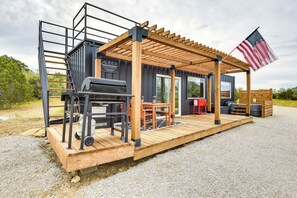 A small, modern outdoor structure with a wooden deck, a grill, and a table with chairs.