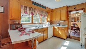 A kitchen with wooden cabinets, a white countertop, a radio, and a window with checkered curtains. - Haysi Nature Getaway w/ Fire Pit & On-site Creek! (Haysi)