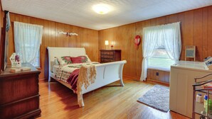 A bedroom with a wooden floor, a bed, a dresser, a washing machine, and a window with curtains. - Haysi Nature Getaway w/ Fire Pit & On-site Creek! (Haysi)