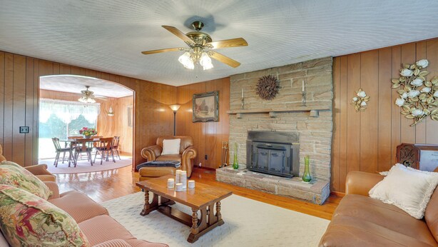 A living room with a fireplace, wooden walls, a ceiling fan, and a dining area with a table and chairs. - Haysi Nature Getaway w/ Fire Pit & On-site Creek! (Haysi)