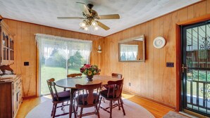 A dining area with a wooden table, four chairs, a ceiling fan, and a large window with sheer curtains. - Haysi Nature Getaway w/ Fire Pit & On-site Creek! (Haysi)