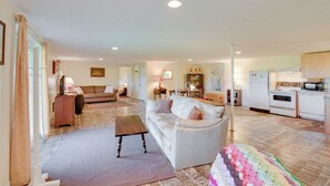 A spacious living room with a white sofa, a wooden coffee table, and a colorful blanket on the floor.