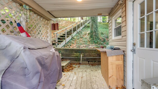 A covered outdoor area with a wooden deck, a covered bench, and a staircase leading to a wooden door. - Horseshoe Lake Vacation Rental w/ Deck & Kayaks! (Batavia)