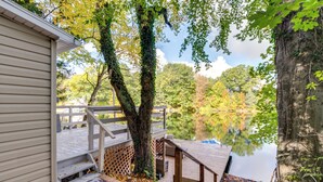 A wooden deck leading to a lake, surrounded by trees and a building with a white exterior. - Horseshoe Lake Vacation Rental w/ Deck & Kayaks! (Batavia)