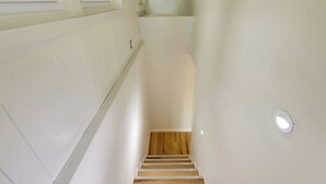 A staircase with wooden steps and white walls, leading to a landing with a window. - Horseshoe Lake Vacation Rental w/ Deck & Kayaks! (Batavia)