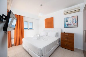 A hotel room with a bed, a wooden dresser, a television mounted on the wall, and a window with curtains.
