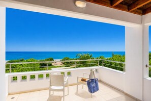 Un balcon avec vue sur la mer, une chaise, une table et un sac bleu.