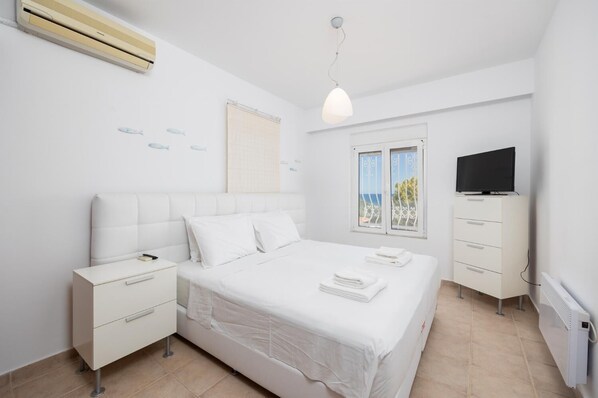Ein Schlafzimmer mit Bett, Nachttisch, Kommode, Fernseher und einem Fenster mit Blick.