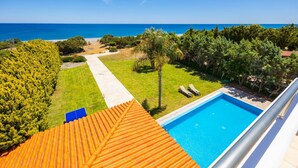 A rooftop pool with a clear view of the ocean, a pathway leading to the beach, and lush greenery surrounding the area.