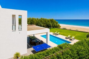 A modern house with a swimming pool, outdoor seating, and a view of the beach.