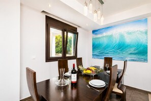 Un coin repas avec une grande table, des chaises, une bouteille de vin et un panier de fruits.