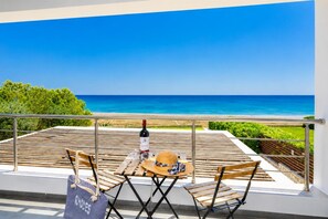 A balcony with a view of the sea, a bottle of wine, and a hat on a table.