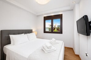 A hotel room with a bed, a TV, a window with a view, and a wooden floor. - Villa Lahania - Three Bedroom Villa, Sleeps 6 (Rhodes)