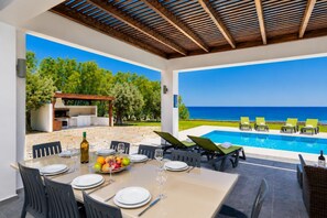 Un espace extérieur aménagé pour les repas, avec une piscine et des chaises longues, un barbecue et une vue sur la mer.