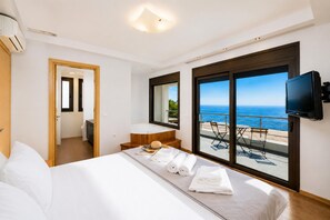 A hotel room with a bed, a TV, a balcony with a view of the sea, and a bathroom.