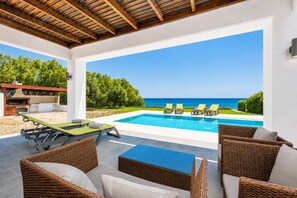 Un espace aménagé au bord de la piscine, avec des meubles en osier, un barbecue et une vue sur la mer.