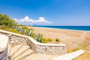 Una escalera de piedra que lleva a una playa, con vista despejada al mar y montañas a lo lejos.