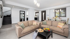 Ein modernes Wohnzimmer mit einem beigefarbenen Ecksofa, einem Couchtisch mit Obst und einer Treppe, die in einen anderen Raum führt.