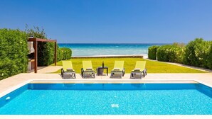Ein Swimmingpool mit Meerblick, umgeben von grünen Hecken und einer Pergola.
