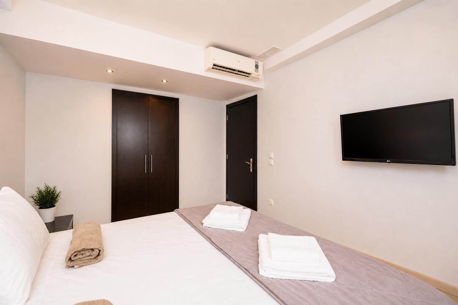 Ein Hotelzimmer mit Bett, Wandfernseher, Kleiderschrank und Klimaanlage.