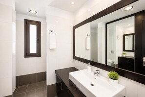 A modern bathroom with a large mirror, white sink, dark tiles, and a small plant. - Villa Tsampikos - Three Bedroom Villa, Sleeps 6 (Rhodes)
