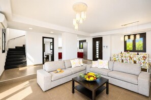 A modern living room with a sectional sofa, a coffee table with fruit, a staircase, and a kitchen in the background.