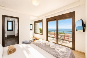A bedroom with a bed, a window, a TV, and a balcony with a view of the sea.