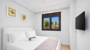 Een slaapkamer met een bed, kussens, een gewatteerde deken, een raam met uitzicht en een wandtelevisie.