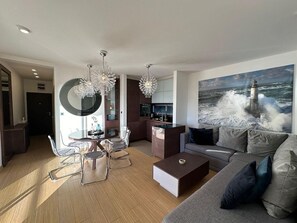 A modern living room with a dining area, a kitchen, and a large ocean view painting. - Sea view Apartments Panorama Przno (Pržno)