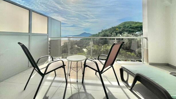 Ein Balkon mit Tisch und Stühlen, der einen Blick auf eine gebirgige Landschaft bietet.