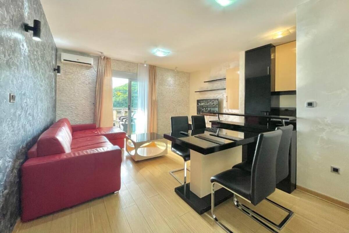 Un salon moderne avec un canapé rouge, une table à manger avec des chaises et un coin cuisine doté d’un plan de travail noir et de placards.