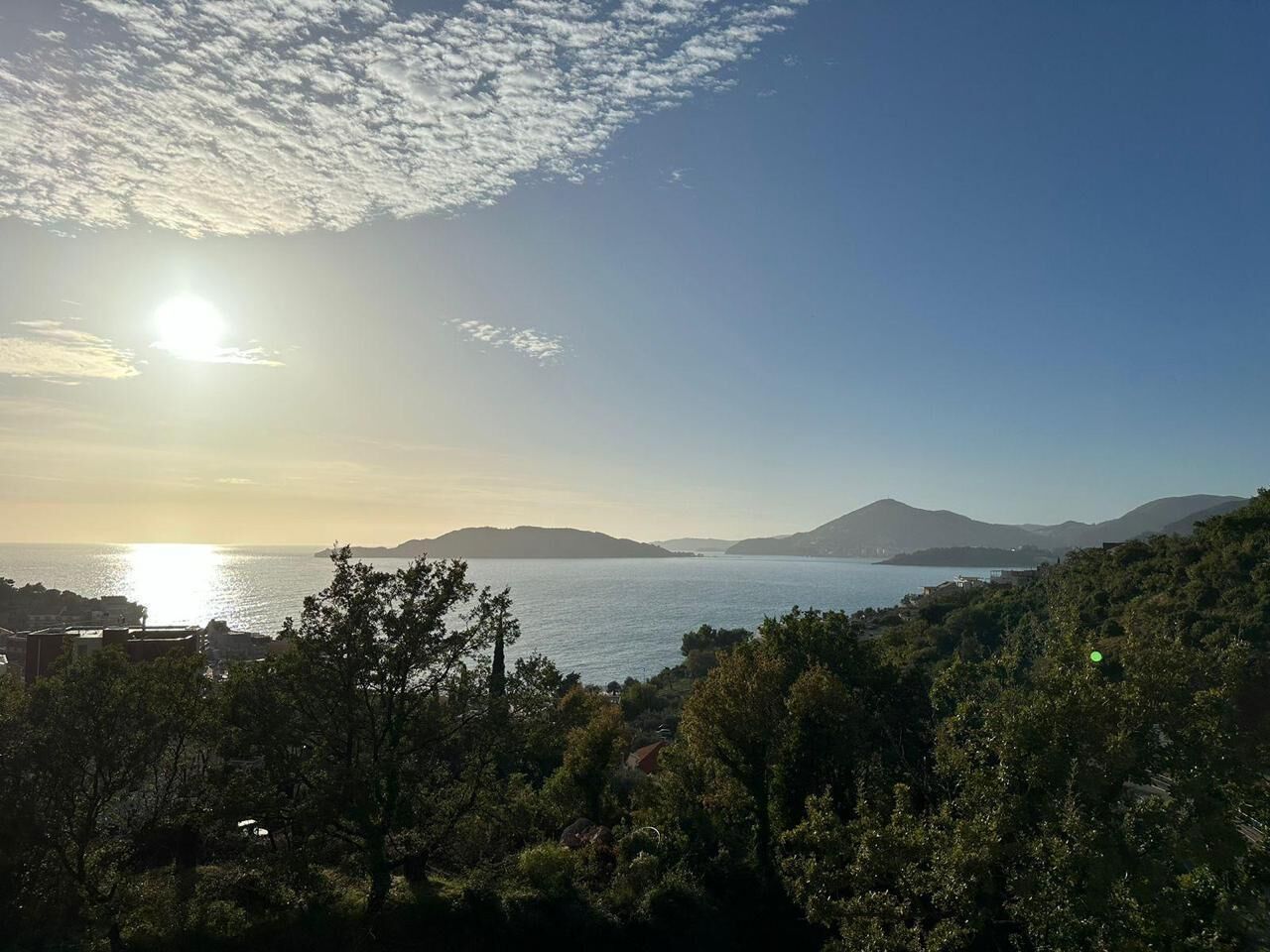 A coastal landscape with a clear sky, a body of water, and distant hills.